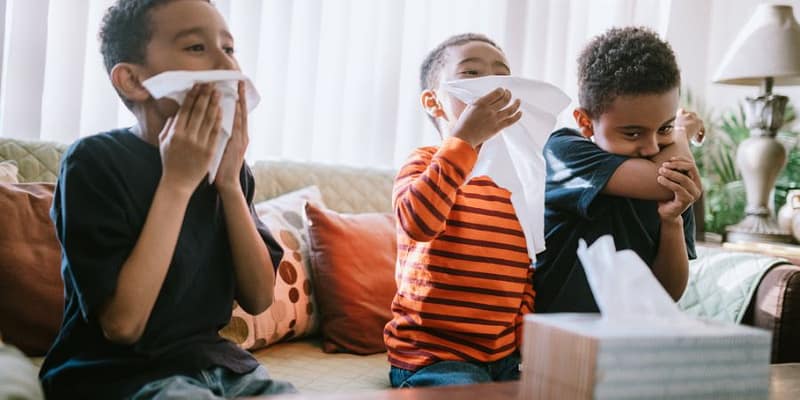 three boys each blowing their nose using a tissue